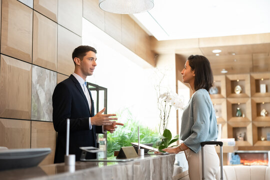 Male receptionist assisting to female guest at front desk, processing check-in, answering questions, explaining booking reservation detail, provide professional hospitality services in hotel reception