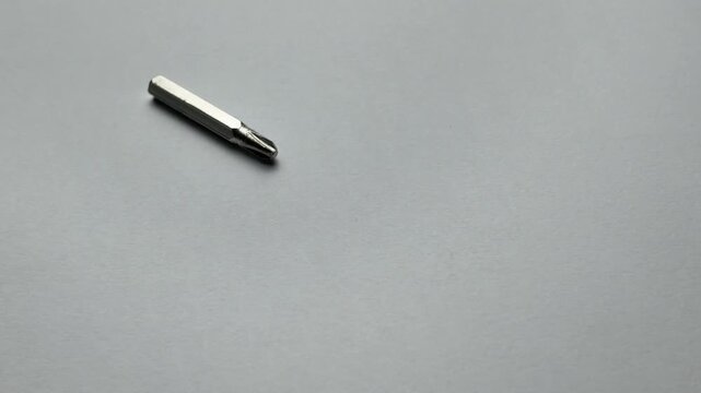 Macro view of several industrial phillips cross head screwdriver bits rolling and scattering on a grey textured background, perfect for hardware store, carpentry, and electrical work concepts.