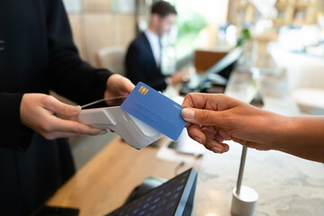 Closeup receptionist holding terminal, customer paying for services tapping her credit card, making...