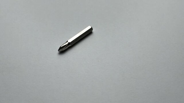 Top down macro shot of silver phillips screwdriver bits dropping onto a clean grey paper background, showcasing various magnetic tips and hex shanks used for construction and DIY repair.