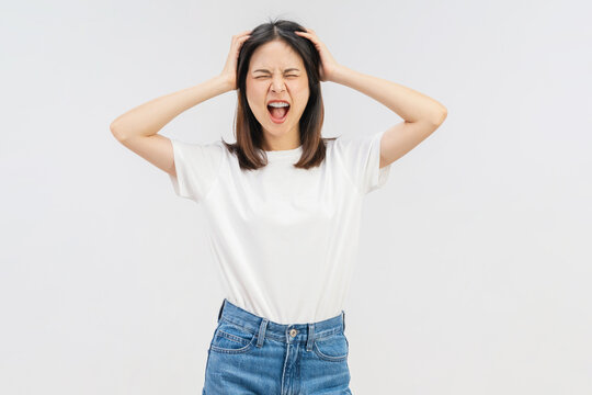 Stressed young Asian woman holding her head and screaming with frustrated expression isolated on white studio background.