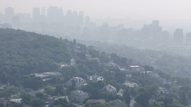 Hazy aerial view of Westmount and downtown Montreal skyline hidden behind smog and trees. c.