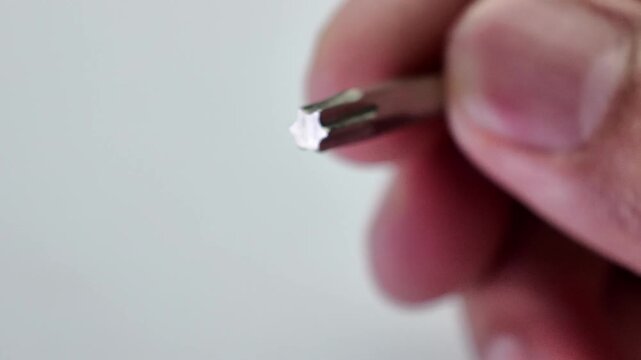 Top down macro shot of a hand carefully placing a metallic star shaped torx screwdriver bit onto a flat neutral grey paper surface next to other hardware parts.