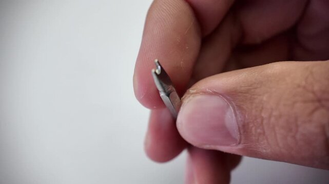 Close up shot of a technician's hand sorting through various slotted flat head steel screwdriver bits on a plain gray studio workbench background.