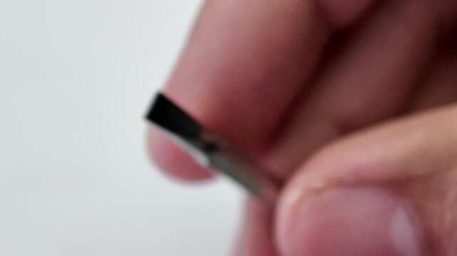 Top down view of a hand reaching out to pick up a double ended phillips screwdriver bit from a gray paper background sheet.