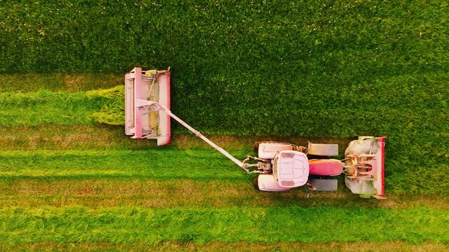 Red dusty tractor mowing grass field with front and side cutter, Europe sunset