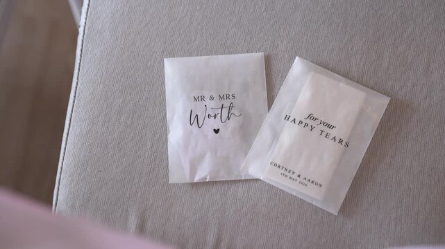 Two packets are placed on a soft surface. One is labeled Mr and Mrs Worth. The other is for happy tears, intended for guests at a wedding for Courtney and Aaron.