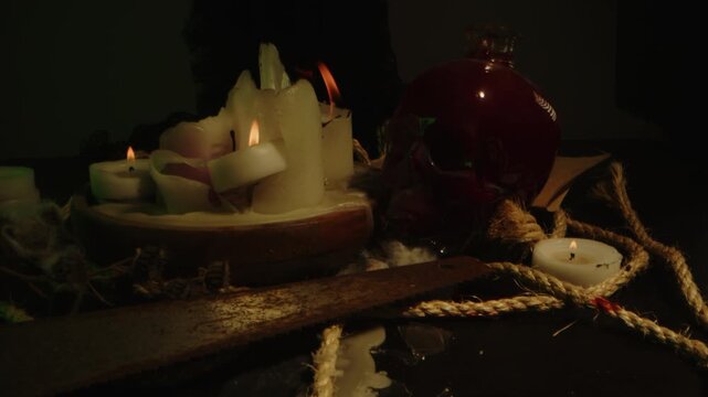 Eerie dolly in of a macabre and occult altar in a dark room. Burning candles, a rusty saw and a blood filled skull are depicted in the macabre setting