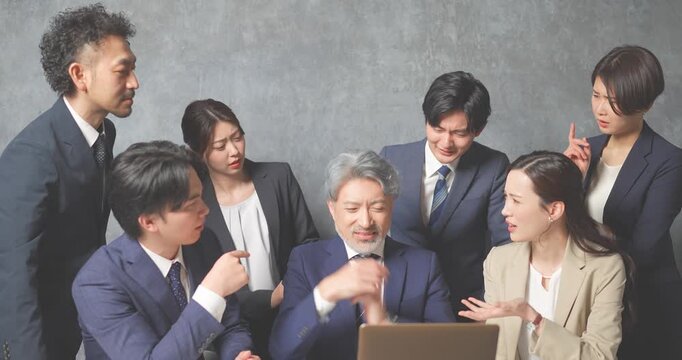 ノートパソコンの前に集合する様々な世代のスーツを着た男女