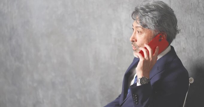 赤いスマートフォンを操作する50代のエグゼクティブ男性