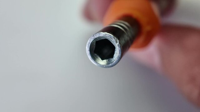 Close up view of fingers holding and displaying a mini precision screwdriver bit on a clean neutral gray studio backdrop.