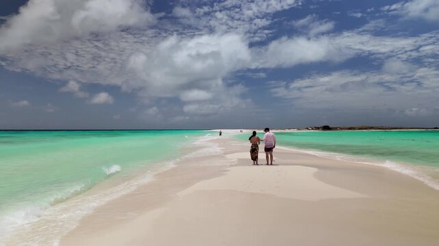 Discover the beauty hidden paradise as couple wanders along remote white sandbar in Cayo de Agua island in Los Roques Archipelago surrounded by crystal-clear turquoise waters.