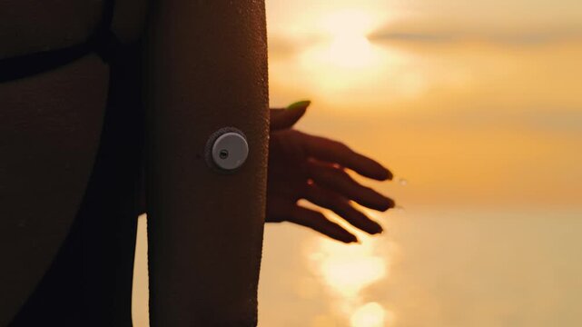 Woman with glucose sensor touching skin at sunset, protection and vulnerability
