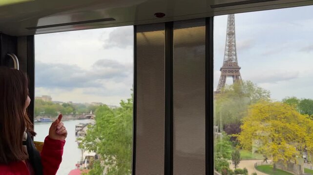 Young female tourist riding the metro in Paris, pointing out the window at the beautiful cityscape and the iconic Eiffel Tower, enjoying her scenic journey through the famous city