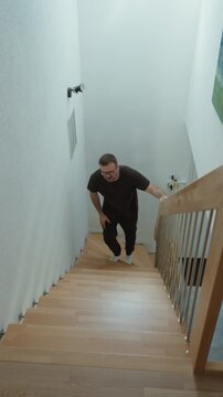 Vertical slow motion video of a man walking upstairs while holding his painful knee, showing joint pain, mobility problems, discomfort, health issues, recovery, and difficulty climbing stairs
