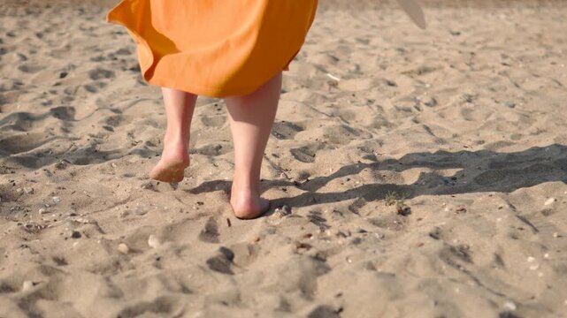 Feet of caucasian woman in dress running on sand towards sea closeup. Movement of person on sunny day during tourist vacation and striving for ocean water on beach.