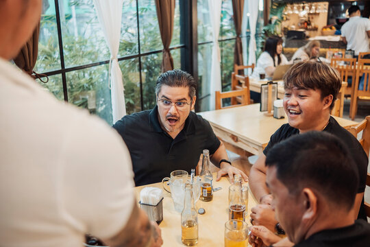A man reacting with surprise with his friends at the bar while drinking beer, receiving an unexpected second round of cold bottled drinks, widening his eyes in shock and excitement