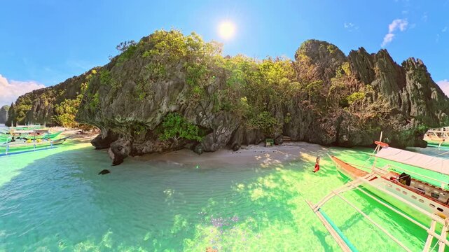 Entalula Beach in El Nido, Philippines, limestone cliffs, vibrant tropical vegetation, and traditional outrigger boats floating on crystal-clear turquoise waters under sunny blue sky of Palawan island