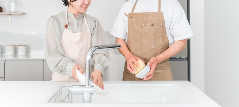 A close-knit Asian couple chatting while doing household chores and washing dishes together in the kitchen of their home.