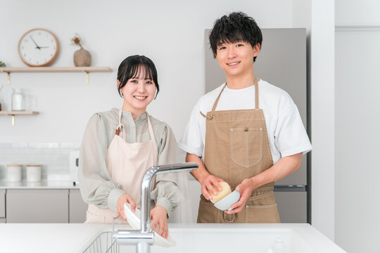 A close-knit Asian couple chatting while doing household chores and washing dishes together in the kitchen of their home.