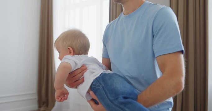 Smiling father gently holding his cheerful baby in a bright modern bedroom, sharing playful family bonding and tender everyday parenting moments