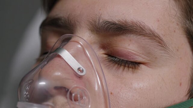 Close-up of a person with closed eyes breathing with the help of a clear oxygen mask, resting peacefully