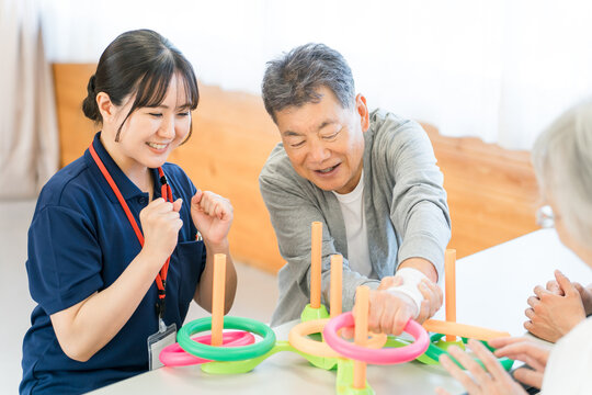 A senior male undergoing rehabilitation, along with a caregiver and a female occupational therapist.