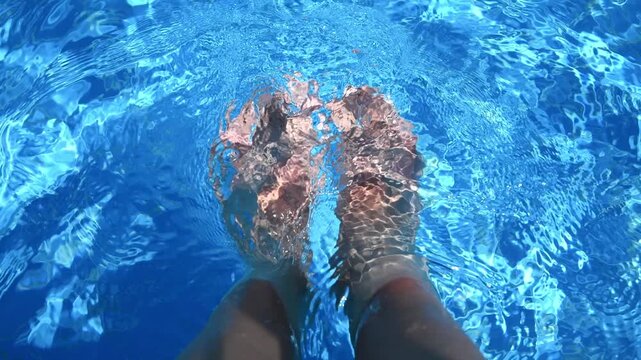 Legs and feet dangling in a refreshing, crystal-clear swimming pool on a sunny day, creating a relaxing and enjoyable summer vacation atmosphere