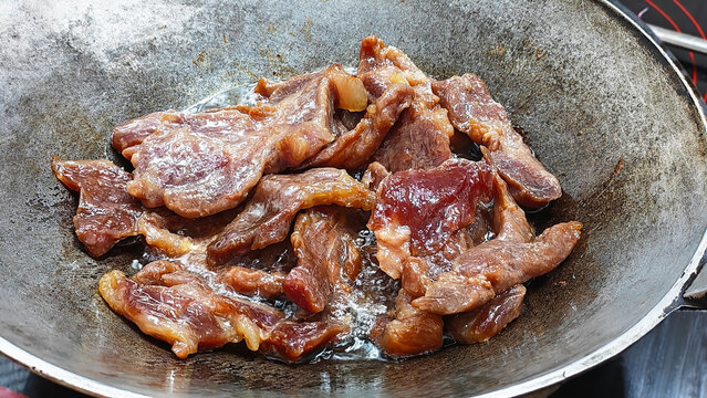 Beef Strips Sizzling in a Pan: Close-up shot of raw beef strips sizzling in a metal pan, ready for cooking. Cooking Thai style sun-dried beef, deep frying marinated sliced beef pieces in a hot iron wo
