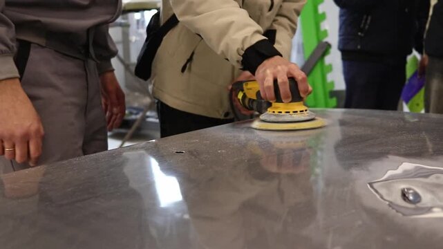 A master polishes a car body in a car repair shop, removing dents and preparing the surface for painting.