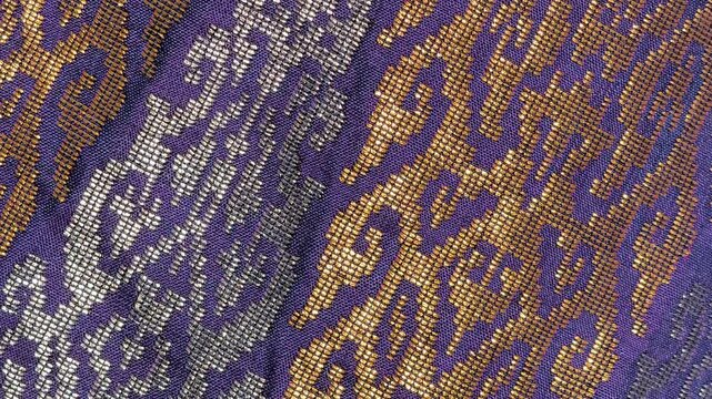 Detailed close-up of luxurious Songket fabric. The intricate gold embroidery shines across the handwoven surface. This prestigious Malaysian textile is reserved for the most special occasions.