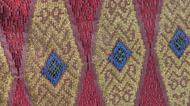 Detailed close-up of luxurious Songket fabric. The intricate gold embroidery shines across the handwoven surface. This prestigious Malaysian textile is reserved for the most special occasions.