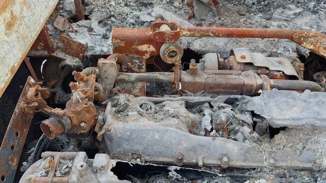 Closeup tracking shot of the burned engine compartment inside a fire-damaged bus showing rusted mechanical parts, melted components, ash, and severe heat destruction aftermath!