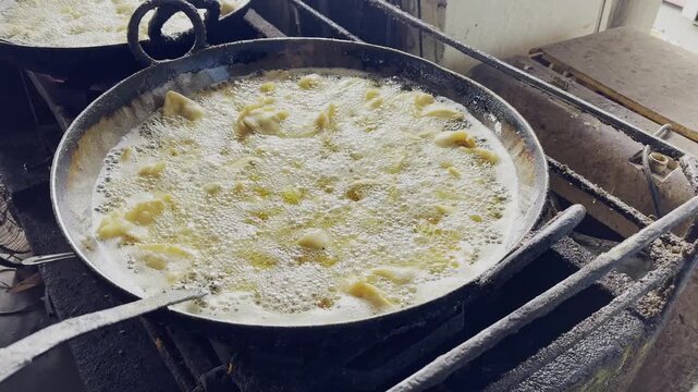 Closeup view of samosas deep frying in bubbling hot oil inside a large iron kadai in a traditional Indian kitchen!