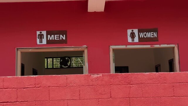 Tilt up shot showing men and women restroom entrance signs above a textured red wall in a public building with simple architectural details and daylight illumination!