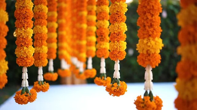 Vibrant orange and yellow marigold flower garlands hanging in vertical rows for a traditional Indian wedding or festival decoration, featuring small white floral accents at the base.
