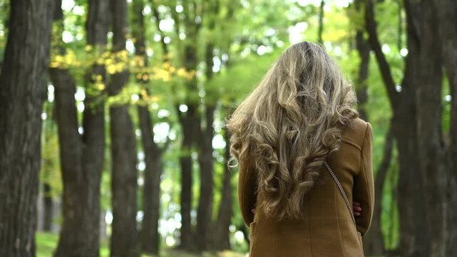 Elegant woman with long wavy hair standing outdoors in park during autumn afternoon.