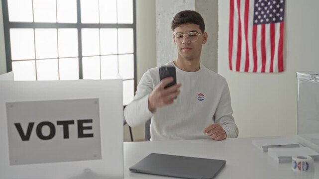 Young man points finger to sticker while taking a selfie with smartphone in a polling station building; civic pride.