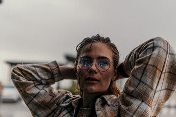 Obraz premium Woman rain glasses standing in heavy rain wearing a plaid shirt and round eyewear during a moody overcast day with copy space