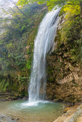 Obraz premium Scenic waterfall cascading down a rocky cliff surrounded by lush green forest in Chakrata, Uttarakhand, India