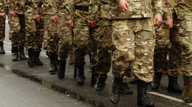 Close-up view of uniformed soldiers in camouflage fatigues marching in tight formation along a wet urban roadway, their boot steps aligned during a coordinated military drill.