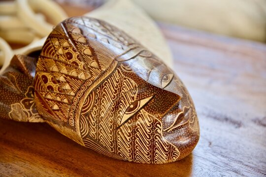Close-up shot of a traditional Indonesian wooden mask decorated with fine batik parang and floral motifs, resting on a rustic wooden table.Opsi 2 (Fokus Kesenian & Budaya): Authentic Javanese handcraf
