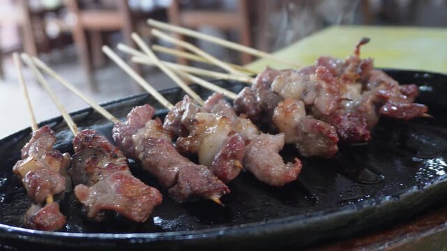 Delicious Sate Klathak, a traditional mutton satay from Yogyakarta, served hot and sizzling on a black hotplate, close-up view.