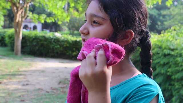 Close up of young Indian girl drinking fresh orange juice during hot summer weather in a green outdoor park, staying hydrated and refreshed while enjoying warm sunny nature.