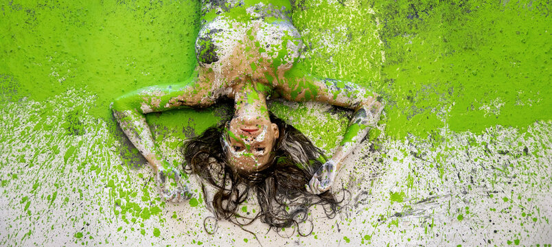 Young woman lying upside down covered in bright green paint splashes expressive body art scene with dynamic texture and bold color creating energetic and playful artistic composition
