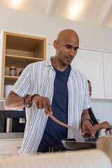 Couple cooking at stovetop in modern kitchen with frying pan and wooden spatula wearing bracelets © wavebreak3