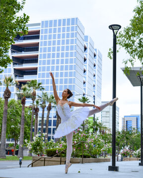 Ballet dancer in white tutu executing dramatic extension outdoors with urban skyline