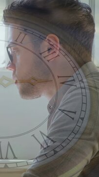 Vertical video: Man sitting at desk by window, business, clock overlay marking time, causing gaze