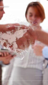 Vertical video: 2 pros reaching, shaking in business, map over hands, 3rd tapping pad, closing deal