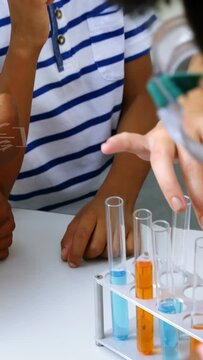 Vertical video: Lead guiding kids with pipette making tube color change in lab with formula on desk